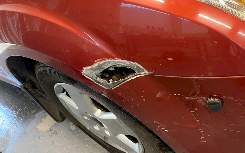 Kuva autosta jossa pelti ruostunut niin että siinä reikä